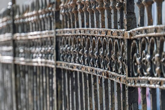 Close-up of an aged, intricately patterned metal grate barred structure, curved design, dark tone, contrasting background, viewed from above in dim lighting, emphasizing its three-dimensionality