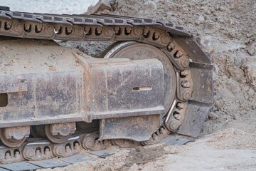Wheeled excavator on muddy terrain, large tires partially sunk, out of focus background with more...
