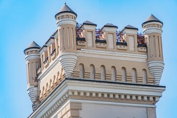 A grand, old stone castle tower in an European city, standing tall against a clear sky, featuring...