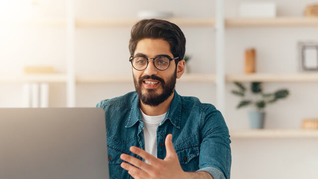 Arab male blogger recording video at home with smartphone on tripod, middle-eastern man making content for his blog, sitting at home office and gesturing at phone camera, copy space - Powered by Adobe