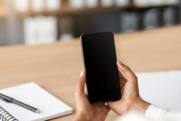 Business woman calls online in office, new normal and social distance. Millennial african american woman sitting at table and looking on smartphone with blank screen, close up, cropped, indoors