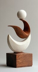 Abstract sculpture of a balanced form.  Two crescent moons, one light, one dark,  rest atop each other, supported by a wooden base. A smooth sphere is positioned between the crescents
