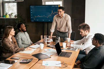 Corporate Meeting Concept. Smiling Male Entrepreneur Giving Speech During Briefing With Coworkers...
