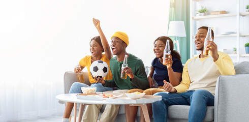 Cheerful black friends young men and women football fans watching game at home, sitting on couch in...