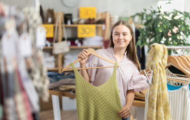Teenage girl buyer choosing summer top in clothing store