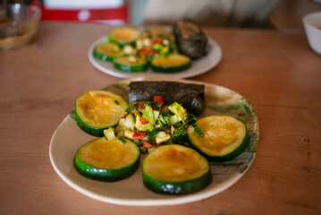 Grilled zucchini slices are served alongside a vibrant avocado salsa and a nori seaweed-wrapped dish, creating a colorful and healthy meal on ceramic plates