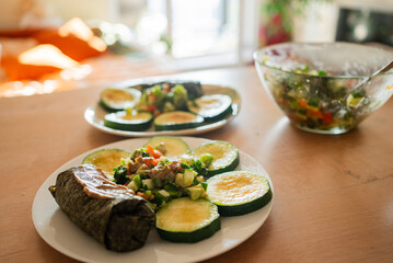 Two plates with grilled zucchini slices, a vegan tamale, and a fresh salad are served on a wooden table, offering a vibrant and nutritious meal