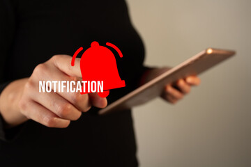 Businesswoman holding a tablet while pointing at a bell icon and the word 