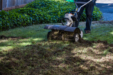 Senior man operating a gas powered dethatching machine, tossing up pieces of dead lawn thatch and...