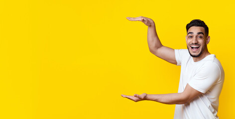 Look what I got. Amazed handsome middle-eastern guy holding something invisible in his hands on yellow studio background, showing his positive emotions, panorama with copy space