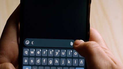 Close-up of hands holding a smartphone while typing ":( sad face" in a messaging app.