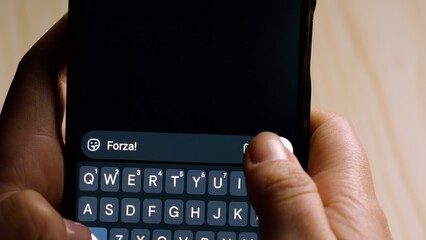 Close-up of hands holding a smartphone while typing "Forza!" (Cheer up!) in a messaging app.
