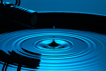 A microphone records the precise sound of a water drop creating ripples in a cinematic blue light setting.