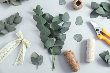 Florist. Eucalyptus branches, threads, pruner and bow on white table, flat lay
