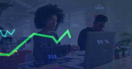 Two professionals analyzing data in open-plan office, with laptop, documents and line graph overlay
