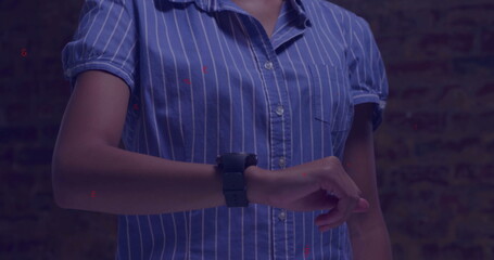 Woman in blue and white pinstripe shirt checking time on black smartwatch against brick wall