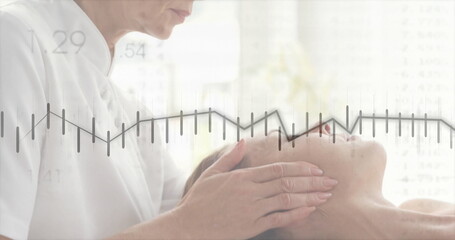 Leaning therapist massaging client face at spa room, with white uniform, padded table and towel