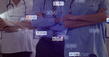 Standing team in medical attire crossing arms in clinic with stethoscopes and social media icons