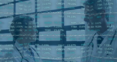 Two doctors analyzing financial data overlay in hospital corridor, with lab coats and stethoscopes