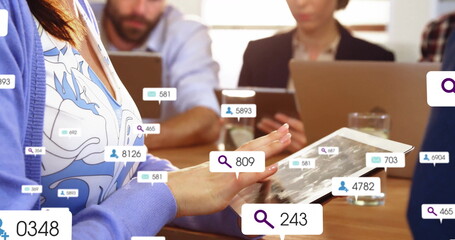 Tapping woman in blue cardigan using tablet at meeting table, with digital UI overlays and laptops