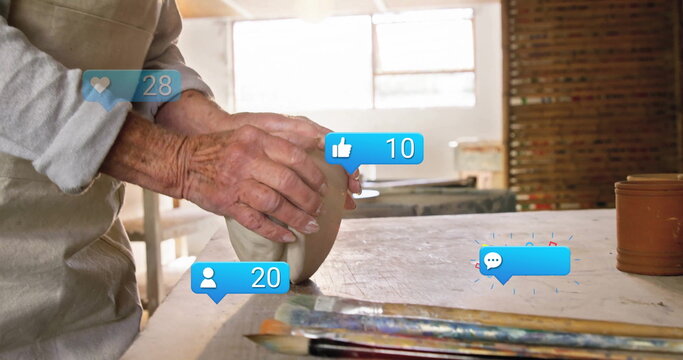 Shaping senior potter wearing apron molding clay vessel in pottery workshop, with digital icons