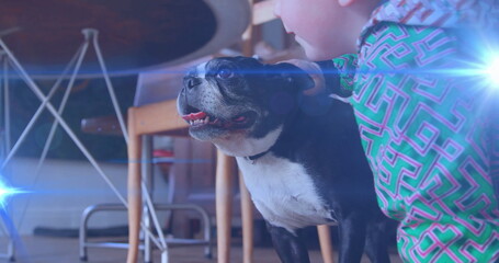 Boy wearing green geometric top kneeling on floor in dining area, petting black-and-white dog