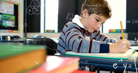 Focusing student in striped sweater writing in notebook at class desk, pencil books bulletin board