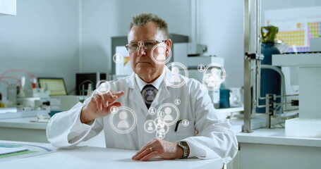 Reaching male scientist wearing lab coat tapping user-avatar icons at bench, periodic table poster