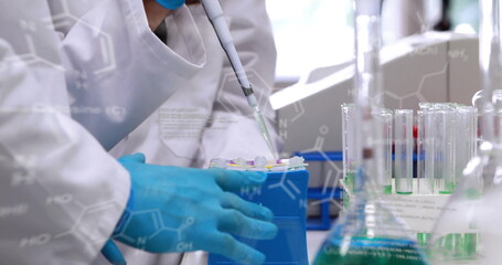 Scientist in lab coat transferring liquid using pipette at bench, with tubes, formulas, copy space