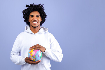 Happy black teenager protecting globe with his hands on blue studio background. Environmental...