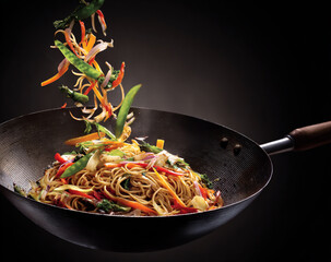 Colorful asian stir fry noodles and vegetables being tossed in a wok isolated on white background