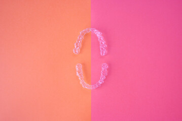 Clear dental aligners and case on two-tone pink background. orthodontic mouthpieces.
