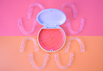 Clear dental aligners and case on two-tone pink background. orthodontic mouthpieces.