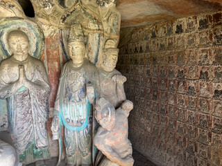 Statues of disciple, Bodhisattva, guardian with small Buddha relief on wall behind in Thousand-Buddha Grotto at Thousand-Buddha Cliff in Guangyuan, Sichuan, China, constructed from late Northern Wei.