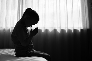 Little child praying next to bedroom window. 