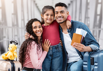 Obraz premium Ready For Vacation. Portrait Of Happy Arab Family Of Three Posing At Airport, Middle Eastern Parents And Cute Female Child With Suitcases And Passports Waiting For Flight At Terminal, Free Space