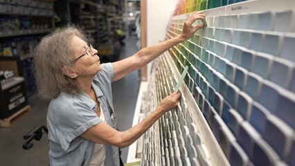An elderly woman in a wheelchair walker browses through paint swatches in a hardware store,...
