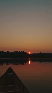 Vertical shot of a canoe on a calm lake at sunset in Algonquin Park with glowing pink skies