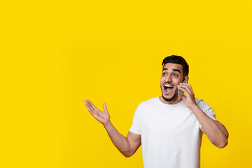Surprised bearded middle eastern millennial guy in white t-shirt having phone conversation with...