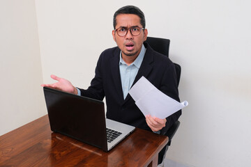 Company manager on his working desk looking at the camera showing confused face expression
