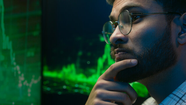 Confident programmer Arabian Indian man looking analyzing computer chart pc graph crypto currency bitcoin IT specialist freelancer male thinking ethnic guy broker trader neon office trading decision - Powered by Adobe