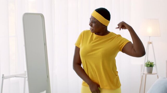 A plus-size woman engages in a fitness routine at home, wearing bright yellow. She stands in front of a mirror, reflecting her commitment to health and body positivity.