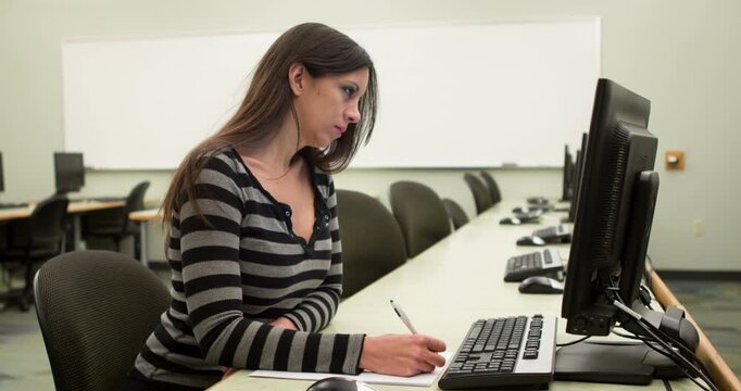 Female working at computer lab desk writing 4k