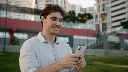 Confident Caucasian young man holding mobile phone smartphone businessman outdoor guy searching...