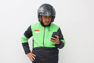 Asian online taxi driver wearing green jacket and helmet using mobile phone while thinking