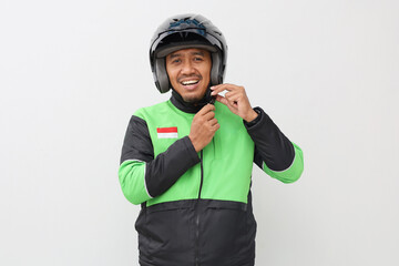Asian man with green jacket standing while wearing black helmet, isolated on white background.