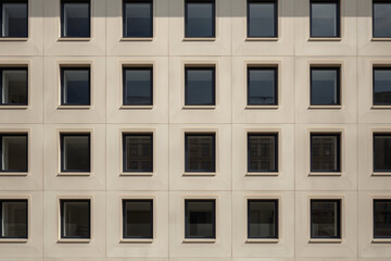 Fototapeta premium Geometric facade with symmetrical window arrangement reflecting urban environment during day