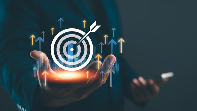 A hand holds a target symbol with arrows indicating growth, symbolizing goal achievement and success in business or personal development.