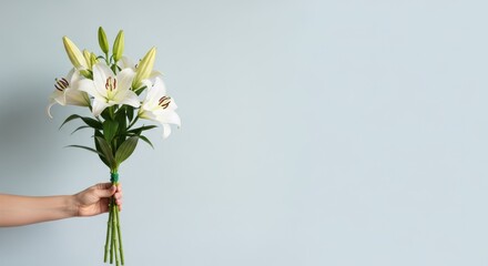 Hand holding a bouquet of white lilies against a light blue background