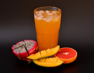 A glass of fruit juice with ice on a black background, next to it are pieces of ripe grapefruit,...